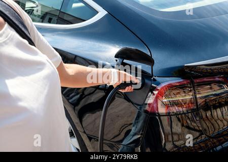 Weibliche Person an einer EV-Ladestation in der Stadt, die ihr Elektroauto auflädt. Saubere Energie und Umweltbewusstsein. Stockfoto