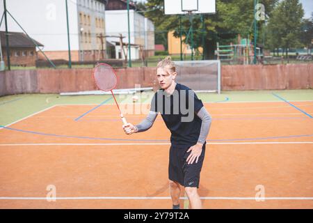 Der Badmintonspieler schlägt während eines Spiels auf einem Platz im Freien den Shuttlecock und zeigt dabei präzise Technik und sportliche Bewegung. Der Spieler fokussiert ist, Stockfoto