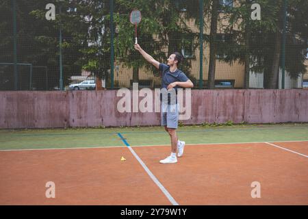 Der Badmintonspieler schlägt während eines Spiels auf einem Platz im Freien den Shuttlecock und zeigt dabei präzise Technik und sportliche Bewegung. Der Spieler fokussiert ist, Stockfoto