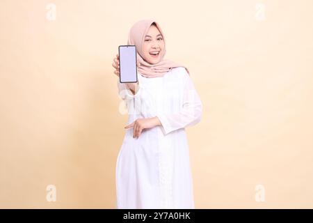 Porträt einer asiatischen muslimischen Frau, die einen Hijab trägt, fröhlich lächelt und ein Handygerät in der Hand hält, mit überkreuzten Armen. Leben Stockfoto