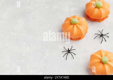 Drei orangefarbene, kürbisförmige Leckereien mit grünen Spitzen, begleitet von kleinen schwarzen Spinnendekorationen Stockfoto