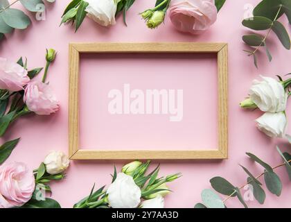 Ein Holzrahmen ist von zarten rosa und weißen Rosen sowie grünen Eukalyptusblättern umgeben und schafft einen frischen und eleganten Anzug mit dekorativen Elementen Stockfoto