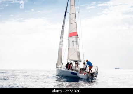 Das Segelboot gleitet über ruhiges Wasser unter klarem Himmel, die Crew arbeitet an Deck Stockfoto