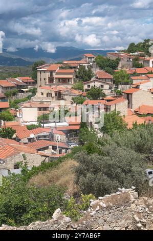 Das Dorf Lofou mit seinen charakteristischen Steinhäusern und roten Ziegeldächern, die sich im Sonnenlicht, das durch die Wolken filtert, mit dem Berg troodos Stockfoto