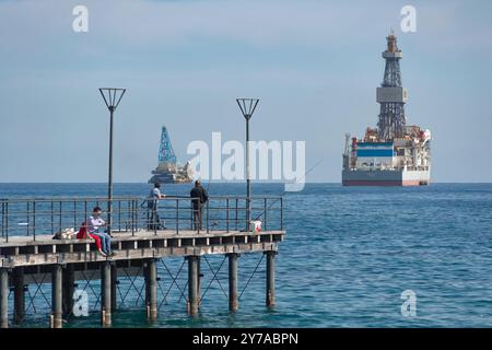 Limassol, Zypern - 5. März 2019: Menschen fischen am Pier mit einer Ölplattform im Hintergrund Stockfoto