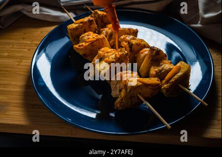 Gegrilltes Hühnchen Ananaskebab auf Spießen mit Gewürzen auf einer blauen Platte auf hölzernem Hintergrund. Stockfoto