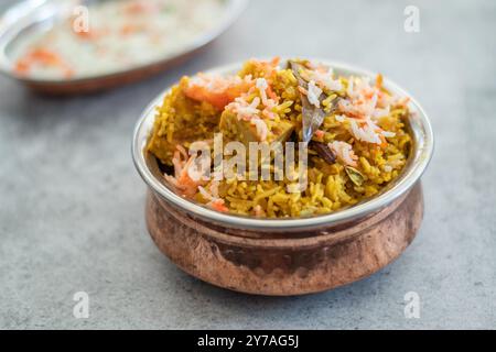 Würziger indischer Biryani-Pulao in goldener Schüssel mit indischem Basmati-Reisgericht mit Hühnerfleisch-Curry Ramadan Kareem, Eid. Servierschale aus Messing mit weißem Rücken Stockfoto