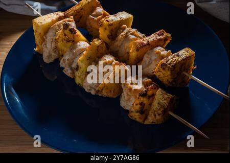 Gegrilltes Hühnchen Ananaskebab auf Spießen mit Gewürzen auf einer blauen Platte auf hölzernem Hintergrund. Stockfoto