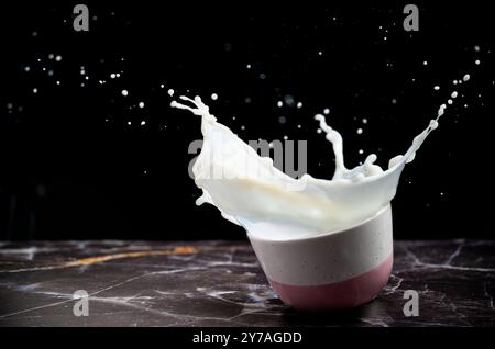 Milchspritzer aus der Schüssel auf schwarzem Hintergrund. Milchkonzept. Milchspritzer aus veganer Pflanzenmilch in der Schüssel. Kopierbereich. Stockfoto