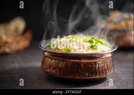 Rauchiger weißer Reis. Zubereitet und in einer Messingschale serviert. Naturholz im Hintergrund. Gebratener Reis in einer Schüssel mit Beilage auf schwarzem Hintergrund. Copysp Stockfoto