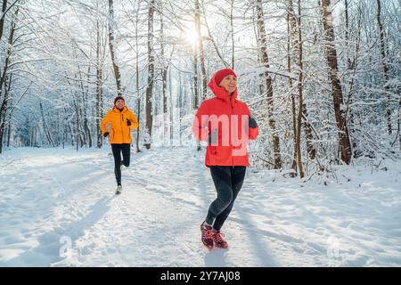 Junge Paare Trailläufer Mann und Frau kleideten helle winddichte Jacken, die während des sonnigen frostigen Tages im malerischen verschneiten Wald laufen. Sportlich aktiv p Stockfoto