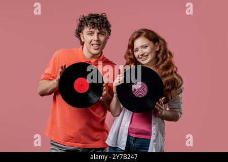 Stilvolles Paar - Mann und Frau tanzen mit Schallplatte auf rosa. Hobby, Musikliebhaber, Sammlung, Nostalgie Lifestyle. Hohe Qualität Stockfoto