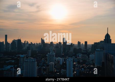 Blick aus der Vogelperspektive auf die Skyline von Bangkok bei Sonnenuntergang mit Silhouette der Wolkenkratzer und der Sonne am Horizont, Thailand Stockfoto