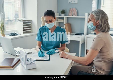 Junge Rettungssanitäterin mit Überwachungsgeräten zur Kontrolle des Reifen Frauenpulses während der Arbeit im Krankenhaus Stockfoto