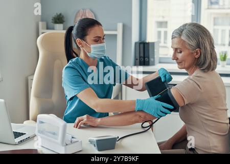 Junge Rettungssanitäterin mit Überwachungsgeräten zur Kontrolle des Blutdrucks bei Reifen Frauen während der Arbeit im Krankenhaus Stockfoto