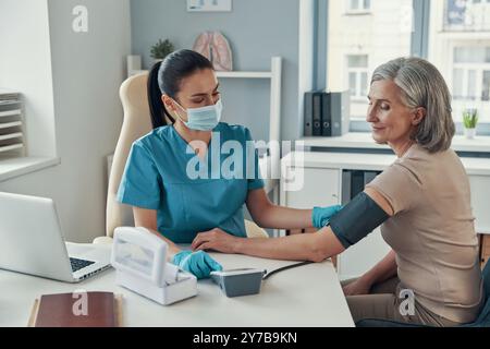 Junge Rettungssanitäterin mit Überwachungsgeräten zur Kontrolle des Blutdrucks bei Reifen Frauen während der Arbeit im Krankenhaus Stockfoto