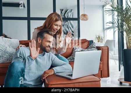 Liebe junge Paare, die einen Videoanruf mit Freunden haben, während sie Zeit zu Hause verbringen Stockfoto