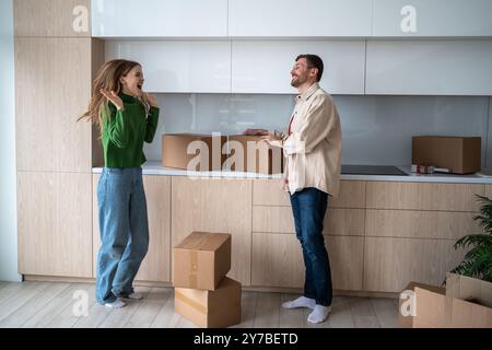 Ein überfröhliches Paar feierte den Umzug in ein neues Haus und sprang mit Pappschachteln von Happy in die Küche Stockfoto