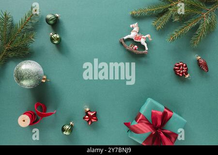 Overhead-Ansicht von eingewickelten Weihnachtsgeschenken, Tannenzweigen, Weihnachtskugeln, Ornamenten und Dekorationen auf grünem Hintergrund Stockfoto