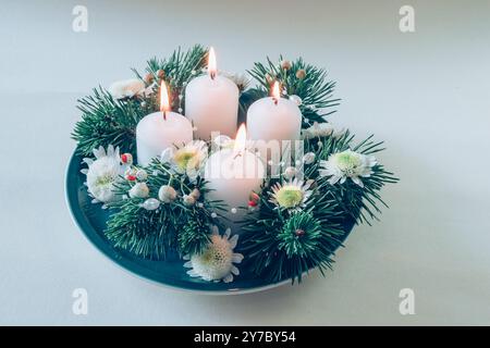 Vier weiße Adventskerzen, Kranzdekor mit Blumen und Kiefer, isoliert, vier Adventskerzen beleuchtet Stockfoto