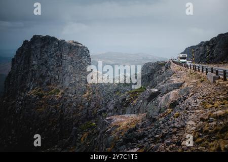 Eine Straße schlängelt sich durch die malerischen Berge der Serra da Estrela unter bewölktem Himmel, wobei die dramatische Landschaft eine stimmungsvolle Atmosphäre schafft. Stockfoto