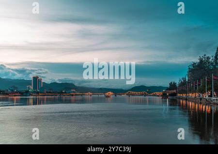 Die alte französische Brücke auf dem Praek Tuek Chhu Fluss in Kampot in Kambodscha bei Sonnenuntergang mit einem beleuchteten Schiff Stockfoto