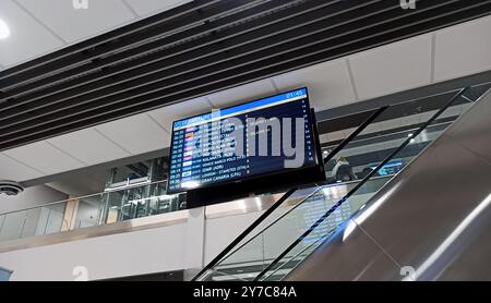 Ein digitales Abflugbrett in einem Flughafen zeigt Flugpläne, Flugsteige und Verspätungen an. Das Bild wurde in der Nähe einer Rolltreppe aufgenommen und zeigt eine moderne, gut beleuchtete Stockfoto