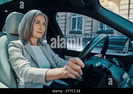 Reife schöne Frau in eleganter Freizeitkleidung lächelt beim Autofahren Stockfoto