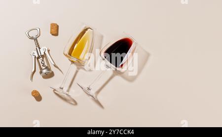 Zwei Weingläser neben einem Korkenzieher und mehreren Korken, alle auf einem hellen Hintergrund angeordnet. Das harte Licht erzeugt scharfe Schatten, die dramatisch wirken Stockfoto
