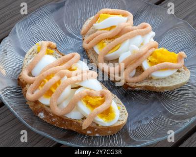 Zwei wunderschön gefertigte Sandwiches mit Eierscheiben und Kaviar im schwedischen Stil ruhen auf einer Glasplatte, die in einer Seitenansicht aufgenommen wird, um die Schichten von hervorzuheben Stockfoto