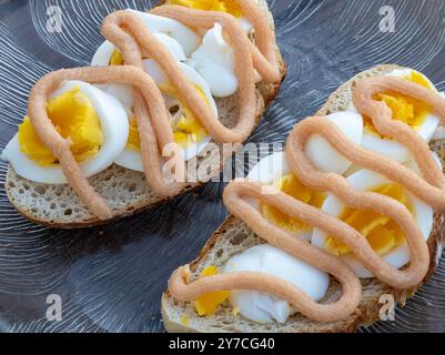 Zwei wunderschön gefertigte Sandwiches mit Eierscheiben und Kaviar im schwedischen Stil ruhen auf einer Glasplatte, die in einer Seitenansicht aufgenommen wird, um die Schichten von hervorzuheben Stockfoto