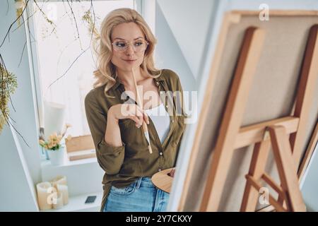 Attraktive junge blonde Frau malte im Kunststudio und sah nachdenklich aus Stockfoto