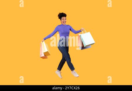 Glücklicher Shopper, der mit bunten Taschen auf einem hellgelben Hintergrund springt Stockfoto