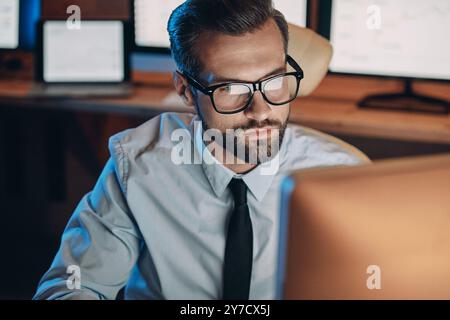 Ernsthafter junger Mann, der am Computer arbeitet, während er lange im Büro bleibt Stockfoto