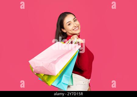 Eine junge Frau strahlt vor Freude und zeigt lebendige Einkaufstaschen in verschiedenen Farben Stockfoto