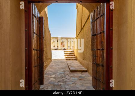 Blick durch die dekorierten Holztüren auf die Innenhof-Türme und Mauern der arabischen Zitadelle Festung, Bahla, Sultanat Oman Stockfoto