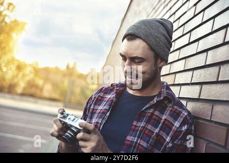 Lächelnder Mann mit retro Foto Kamera Mode Reisen Lebensstil im Freien gegen Mauer Hintergrund Stockfoto