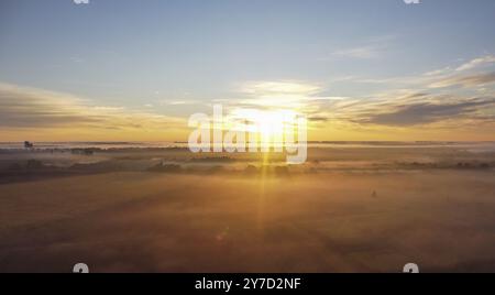 Morgennebel, Sonnenstrahlen und lange Schatten im Nebel, der sich zwischen den Bäumen im Tal in der Nähe des Dorfes erstreckte Stockfoto