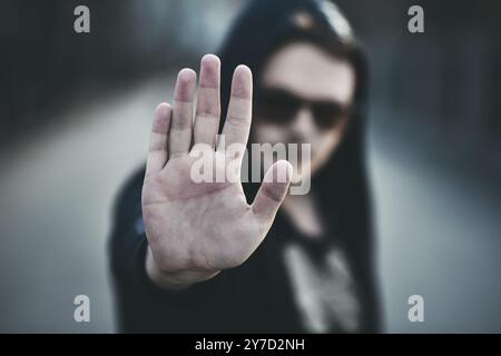 Porträt eines Modemannes in einem schwarzen Pullover mit Kapuze und Sonnenbrille, Handgesten Stockfoto