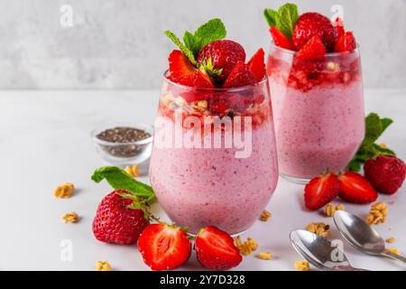 Gesundes Frühstück. Erdbeere-Joghurt-Parfait mit Chiasamen garniert mit frischen Erdbeeren, Müsli und Minze in Gläsern mit Löffeln auf weiß Stockfoto