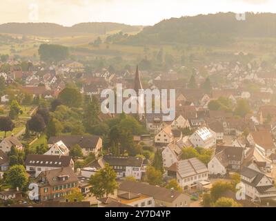 Ein malerisches Dorf mit zahlreichen Gebäuden und einer großen Kirche inmitten einer hügeligen Landschaft aus der Luft fotografiert, Calw, Schwarzwald, Ger Stockfoto