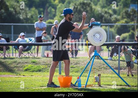 Sault Ste Marie, Ontario, Kanada - 5. August 2024 - Youth Baseball Coach Using Pitching Machine. Fördert Jugendsport, Coaching und Teamarbeit. Stockfoto