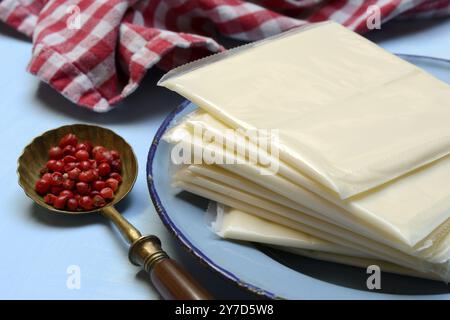 Verarbeiteter Käse, in Kunststoff gewickelte Scheiben von verarbeitetem Käse und Löffel mit rosa Beeren, rotem Pfeffer Stockfoto