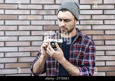 Mann mit Retro-Fotokamera Fashion Travel Lifestyle im Freien beim Stehen vor Backsteinmauerhintergrund Stockfoto