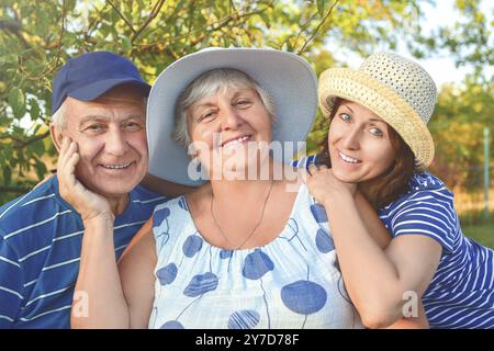 Schönes Seniorenpaar sitzt auf der Bank im Park mit ihrer erwachsenen Tochter. Oma und Opa umarmen und lächeln. Echte Liebe und Familie Stockfoto