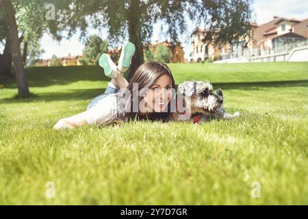 Ziemlich erwachsenen kaukasischen glückliche Frau im Park Ruhe an einem sonnigen Tag mit ihrem geliebten Hund. Weibliche lag auf dem Gras lächelnd und mit Blick auf die Kamera Stockfoto