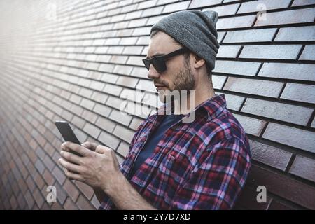 Hipster sms Phone App in Stadt Straße Mauer Hintergrund. Erstaunlicher Mann holding Smartphone in Smart Casual Wear stehen. Urban young profe Stockfoto