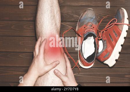 Junger Sportmann mit starken athletischen Beinen, der das Knie mit schmerzhaften Händen hält, nachdem er während eines Lauftrainings auf Woo eine Bandverletzung erlitten hatte Stockfoto