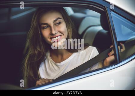 Schöne Frau mit lächelndem Telefon, während sie auf dem Rücksitz im Auto sitzt Stockfoto