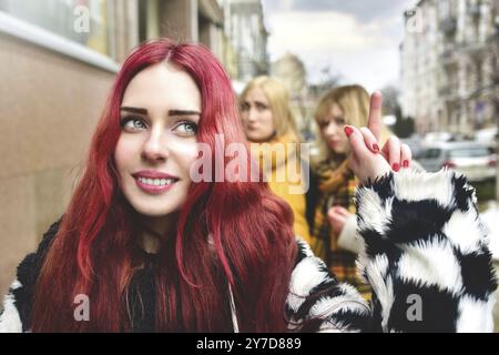 Selbstbewusstes Teenager-Mädchen ignoriert eifersüchtige Menschen, die Klatsch hinter ihrem Rücken verbreiten. Stoppen Mobbing. Soziale Probleme. Ein Mädchen zeigt ihren Mittelfinger t Stockfoto